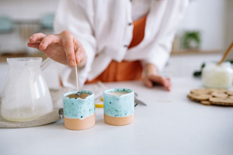 Pouring melted wax into glass candle jars in a small workshop